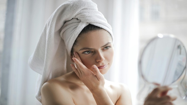 Woman touching her face with a towel on her head, representing self-care and confidence